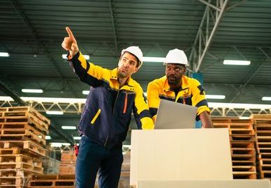 Two warehouse workers discussing logistics and inventory management while collaborating on a project in a storage facility. (Two warehouse workers discussing logistics and inventory management while collaborating on a project in a storage facility., A